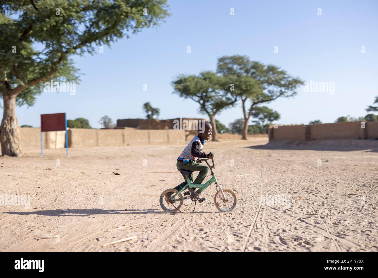 A young boy rides his bicycle on a sandy road in his village in rural Segou Region, Mali, West Africa. 2022 Mali drought and hunger crisis. Stock Photo
