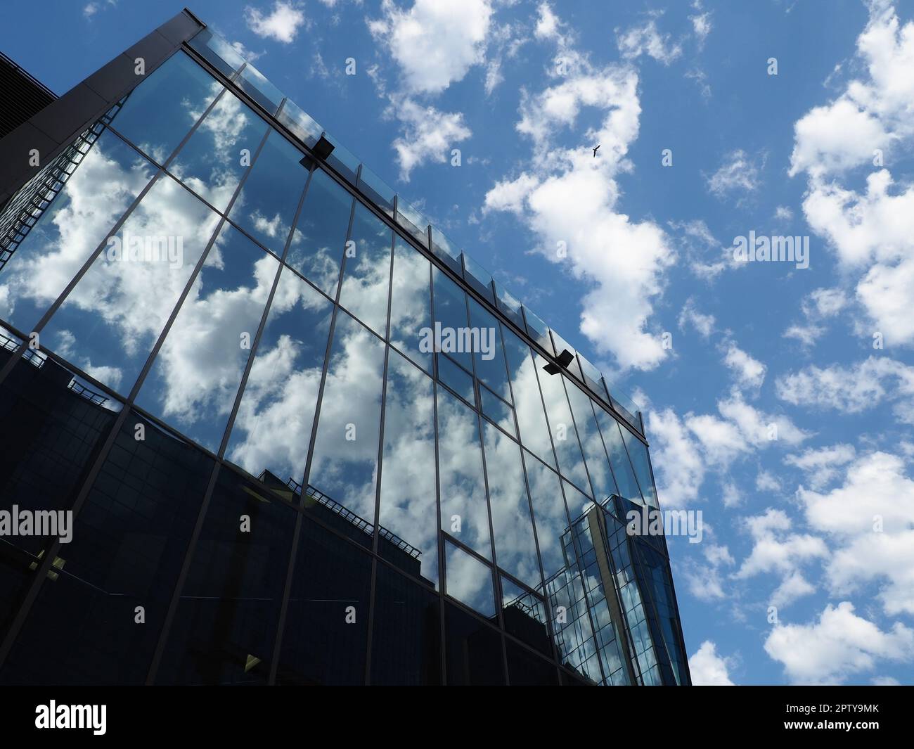 The sky and glass facade of the building. Reflection of the blue sky and white clouds on the glass wall. City skyscrapers. Modern glass buildings and Stock Photo