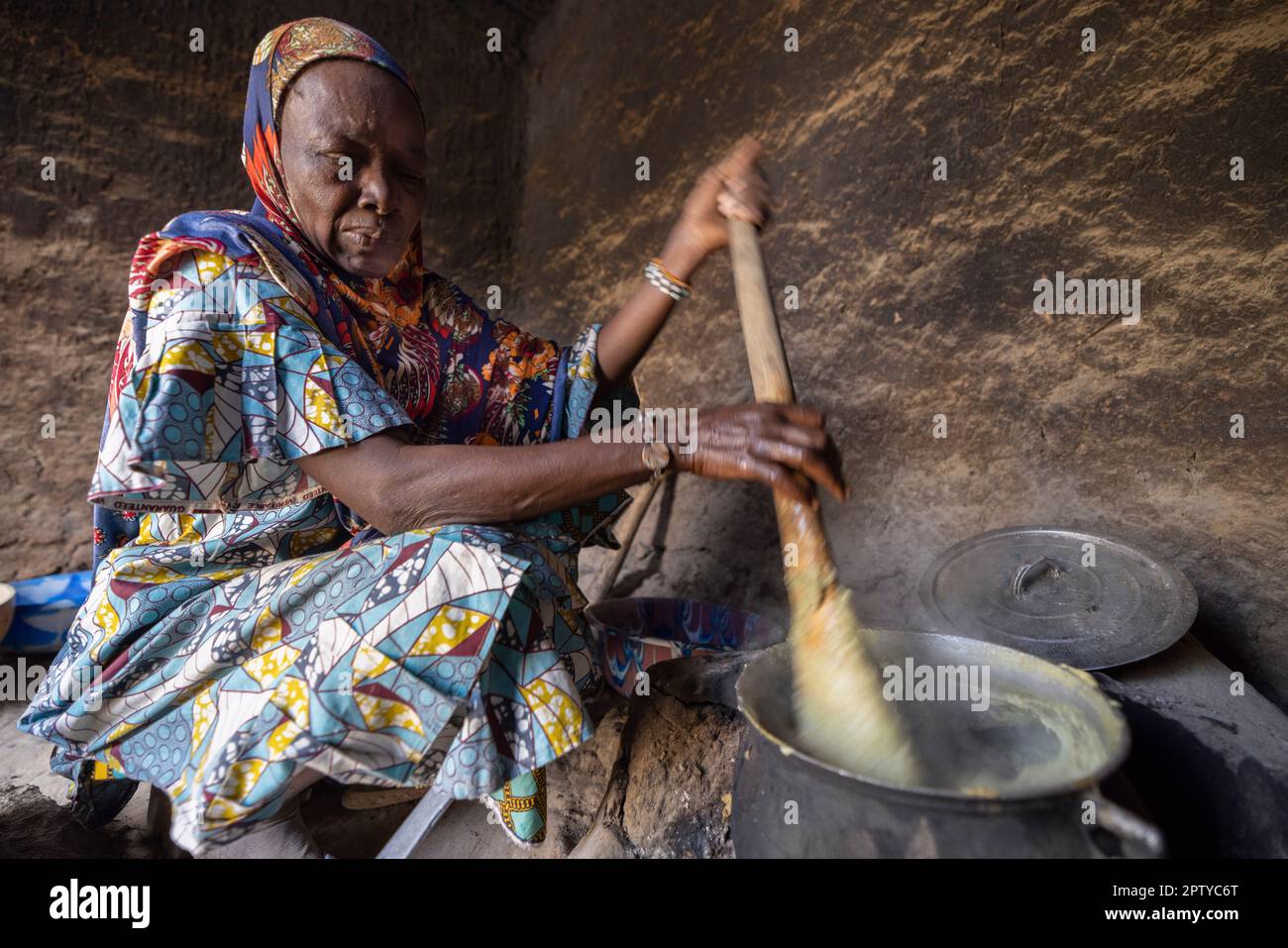 An elderly woman cooks a traditional meal of millet paste over a fire in Segou Region, Mali, West Africa. 2022 Mali drought and hunger crisis. Stock Photo