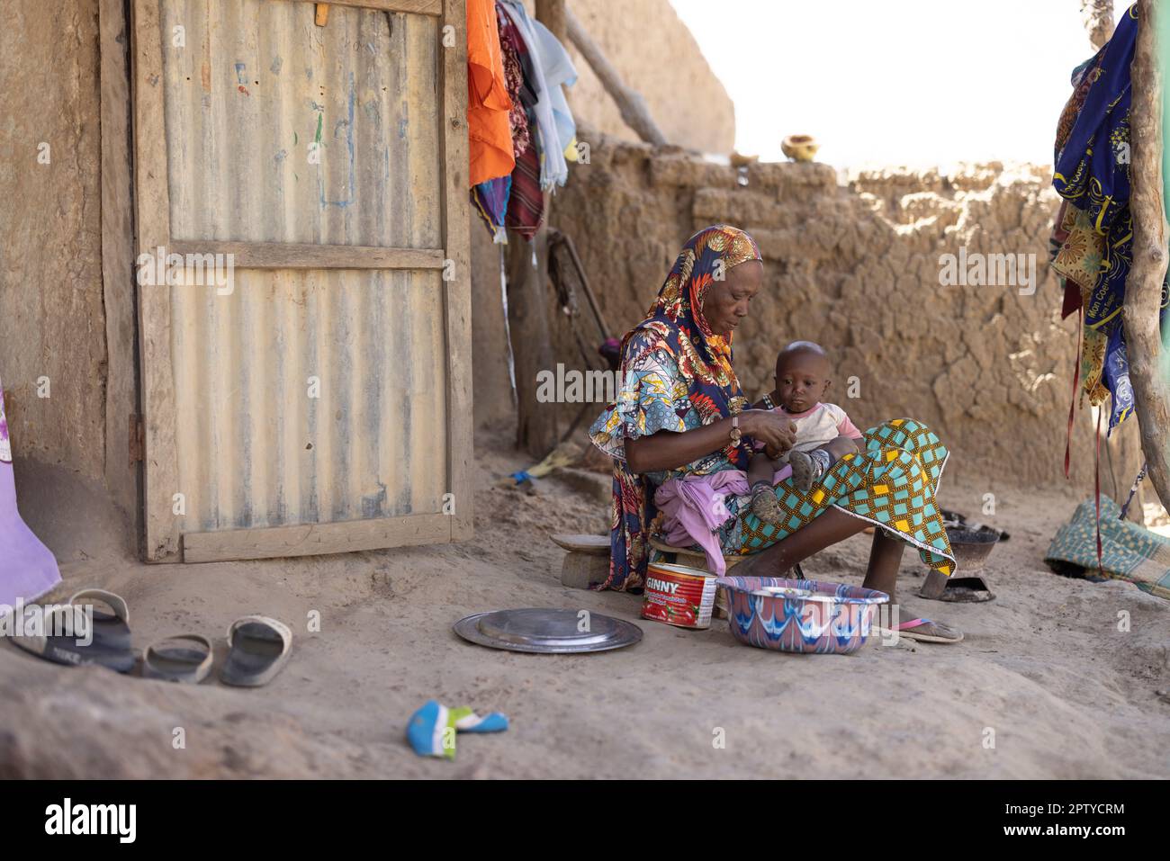 An elderly woman feeds herself and her grandchild outside her mud-constructed home in Segou Region, Mali, West Africa. 2022 Mali drought and hunger crisis. Stock Photo