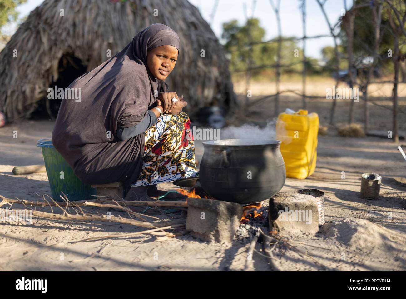 A young Fulani refugee woman, displaced from conflict in the North, boils food over an open fire in Segou Region, Mali, West Africa. 2022 Mali drought and hunger crisis. Stock Photo