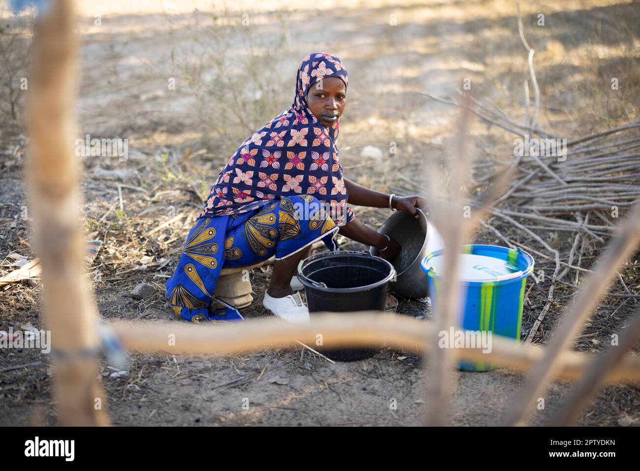 A Fulani woman wearing clean white shoes and traditional dress washes dishes outside her home compound in Segou Region, Mali, West Africa. 2022 Mali drought and hunger crisis. Stock Photo