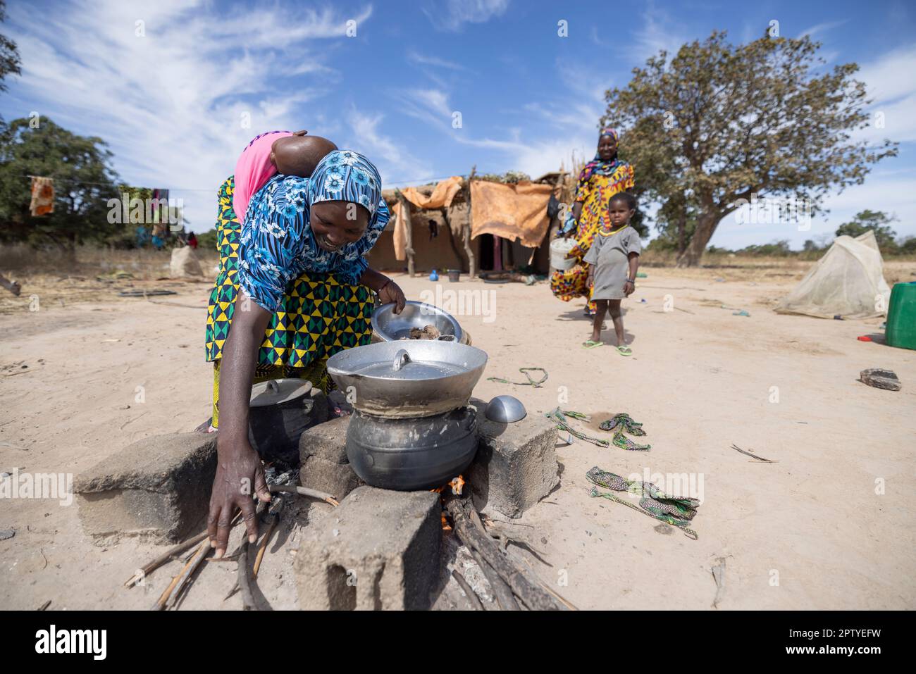Mother cooking a meal over an open fire in front of the family's home in Segou Region, Mali, West Africa. 2022 Mali drought and hunger crisis. Stock Photo