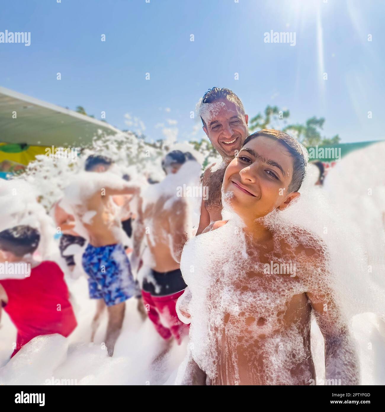 Father and son enjoying a day at the waterpark. Summer concept: Blurred unrecognizable people playing at foam pool party. Kids dancing at dance floor Stock Photo