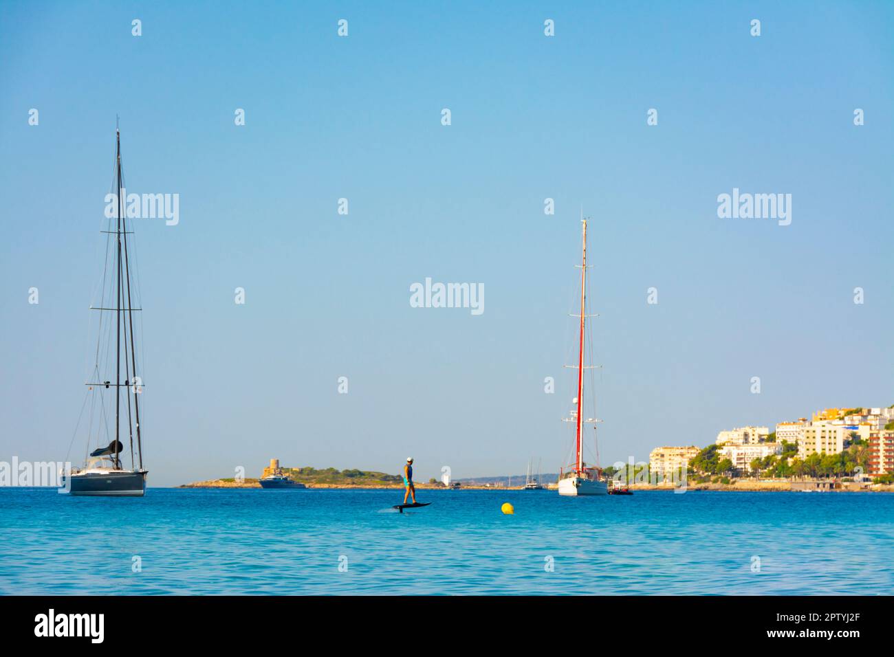Palma, Mallorca, Spain. July 23, 2022 - Apartment buildings, moored sailing boats and man with fliteboard or jetsurf Stock Photo