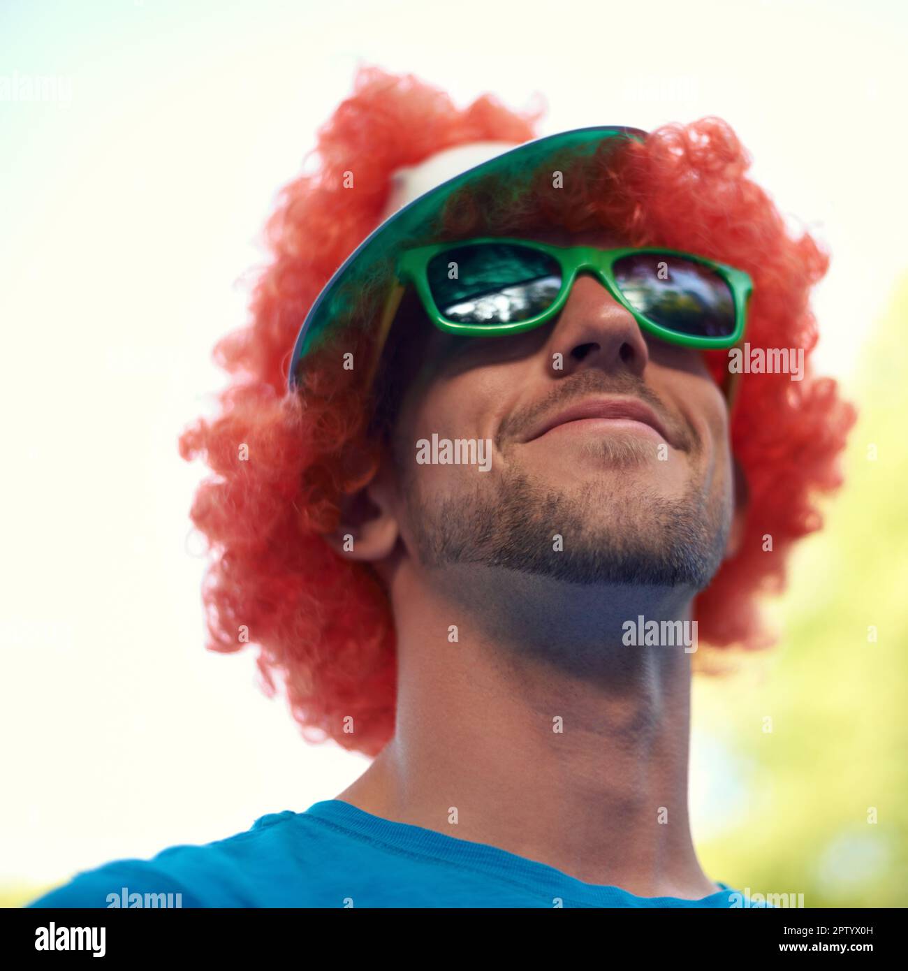 Feeling playful. A young man wearing a playful red wig at an outdoor event Stock Photo
