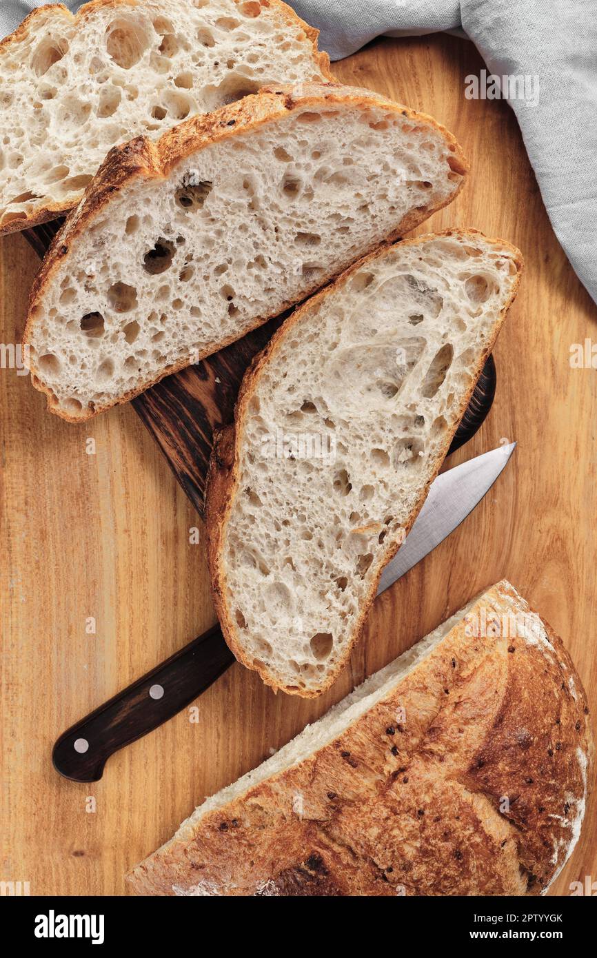 Sliced round rustic bread without kneading on a cutting board next to a knife. Homemade whole grain bread, layout on the table, vertical frame Stock Photo