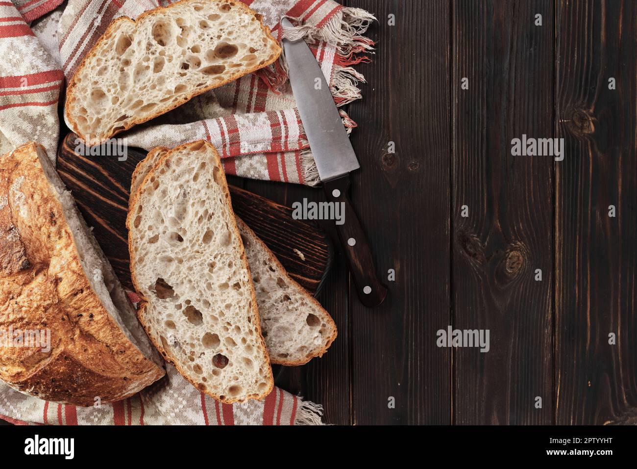 Sliced round rustic bread without kneading on a cutting board on an old rustic table with copy space, dark background. Homemade whole grain bread, lay Stock Photo