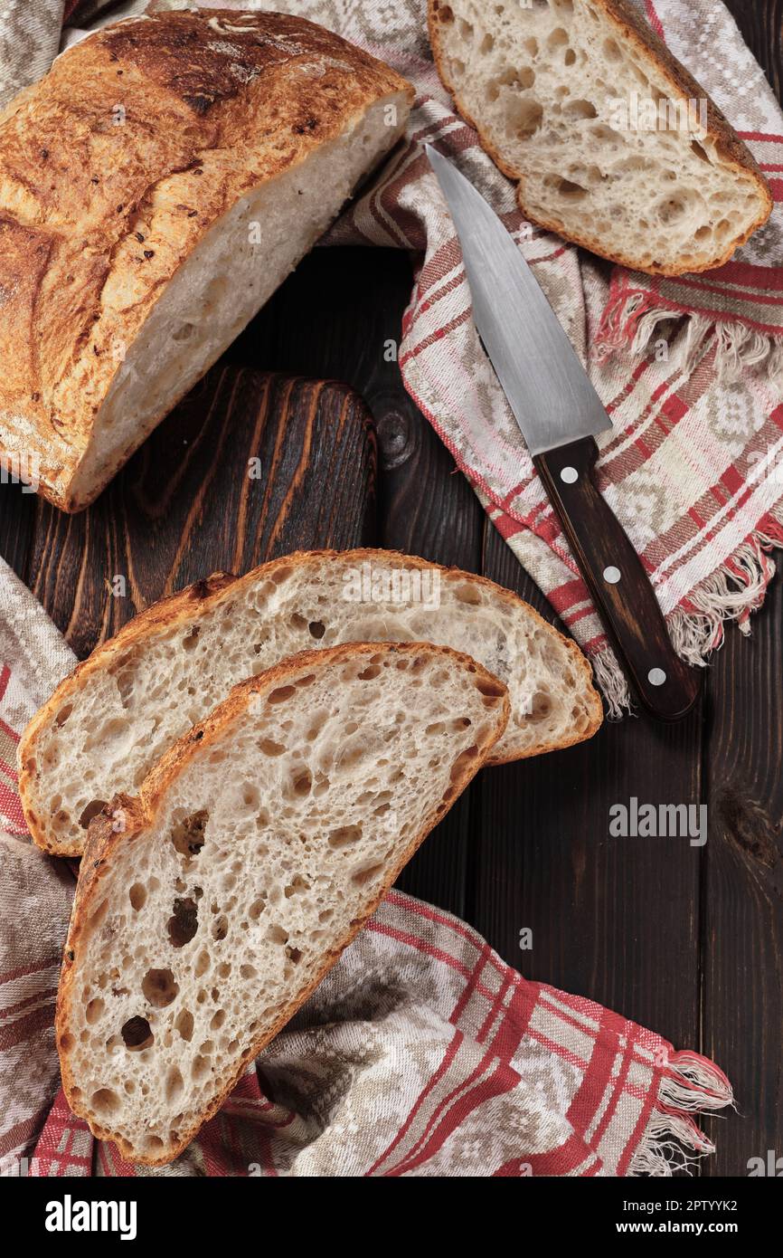 Round rustic bread without kneading cut into pieces on a cutting board on an old dark rustic table. Homemade whole grain bread, layout on the table, v Stock Photo