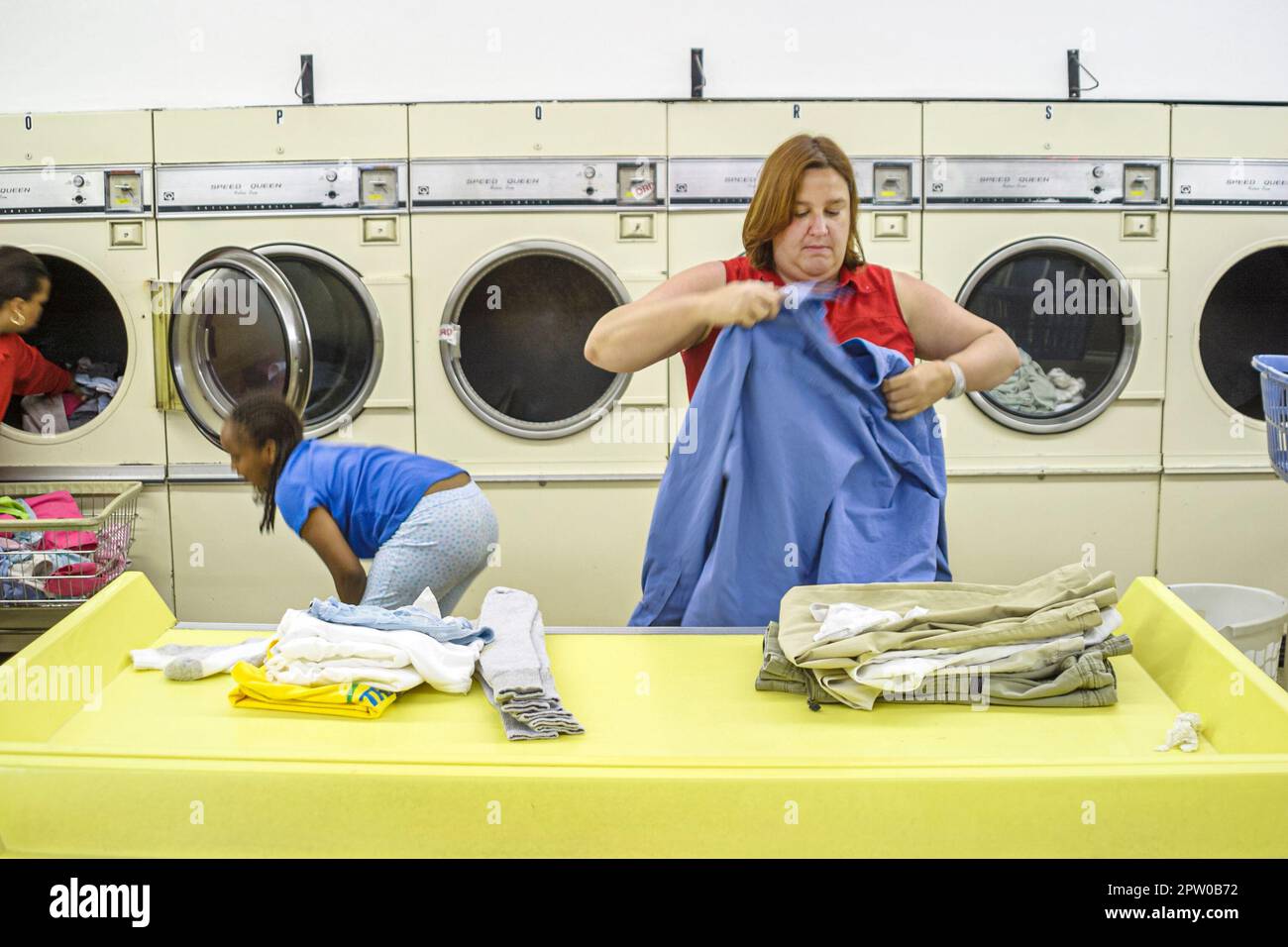 Virginia Roanoke laundromat inside interior washing machines coin-operated,Hispanic Black African Africans,woman female folding folds clothes clothing Stock Photo
