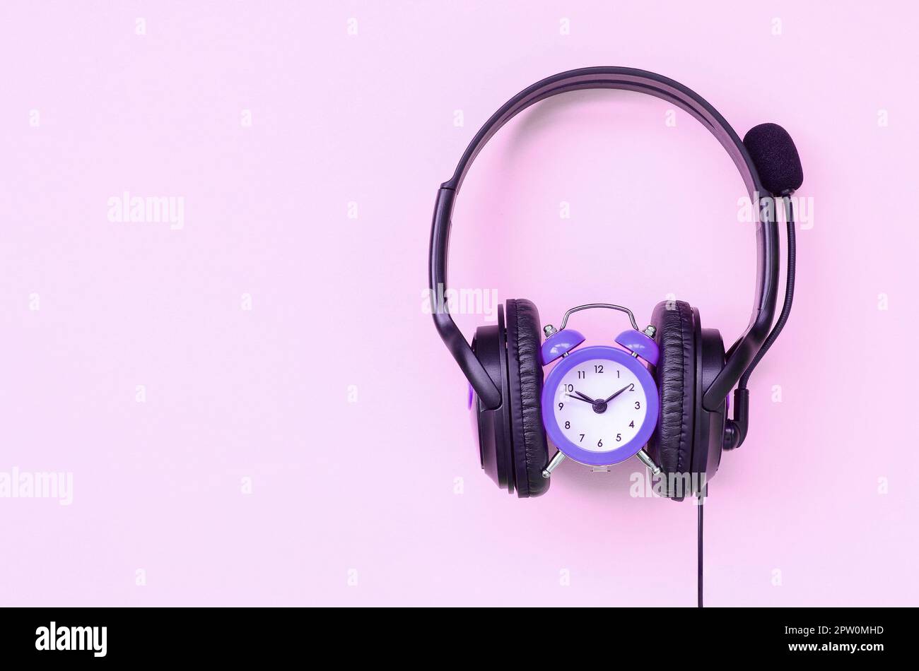 Retro alarm clock with black headphones on pink background. Concept of time to listening music Stock Photo