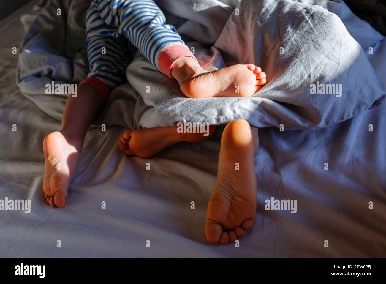 close up view of elder child and smaller child feet in the parent's bed under blanket Stock Photo