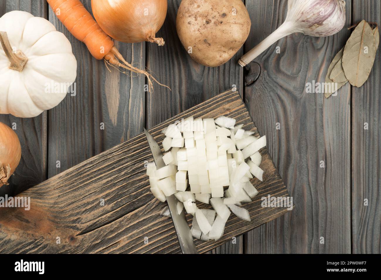 Cutting spicy onion with knife into cubes on kitchen wooden board ...
