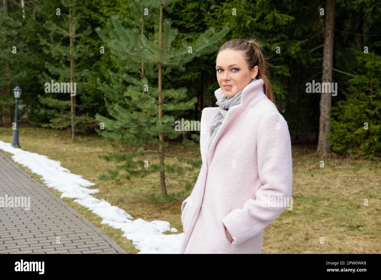 Pretty girl in pink coat walking along pathway in forest Stock Photo