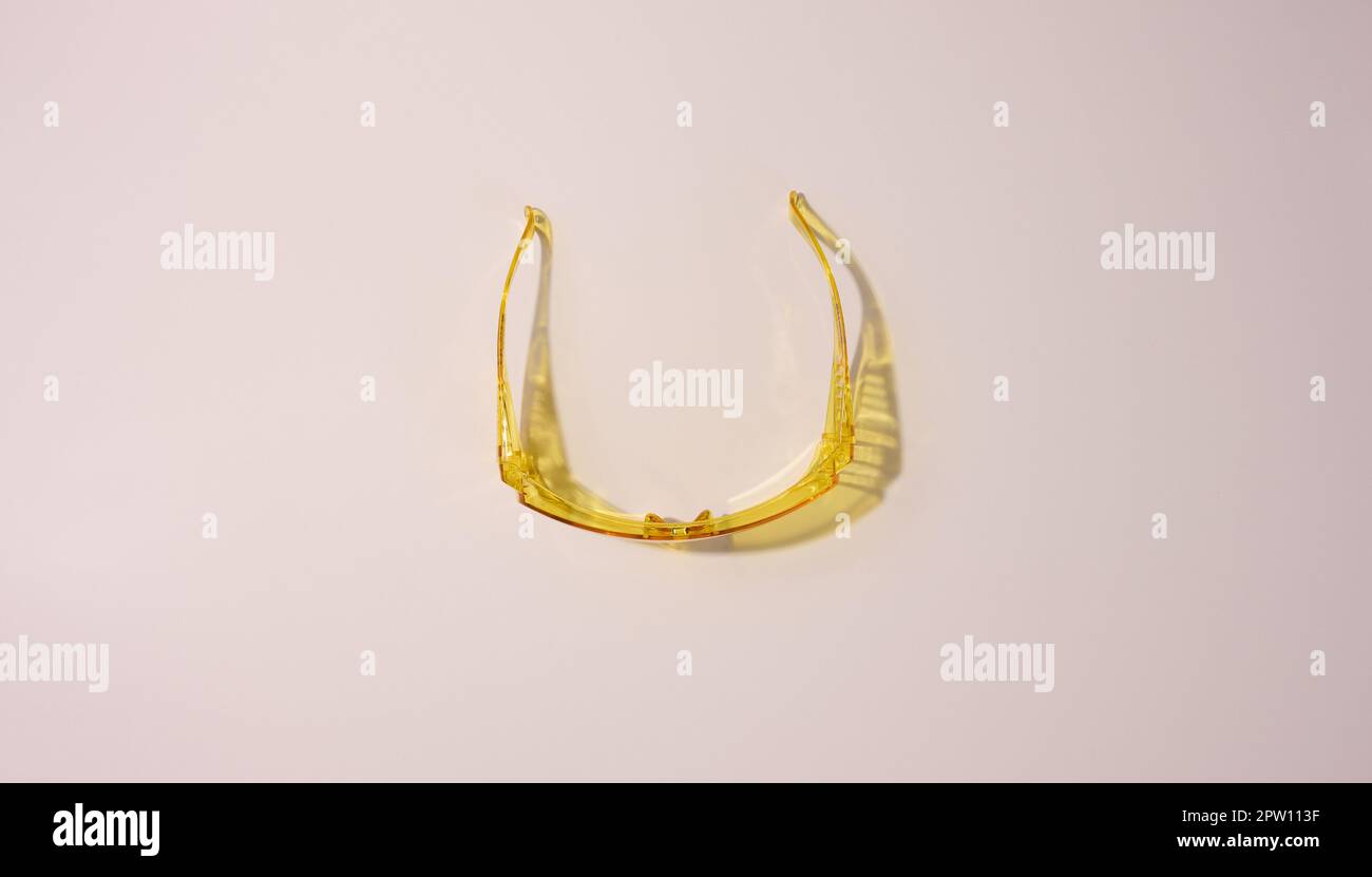 Yellow plastic protective goggles for workers on a beige background, top view Stock Photo