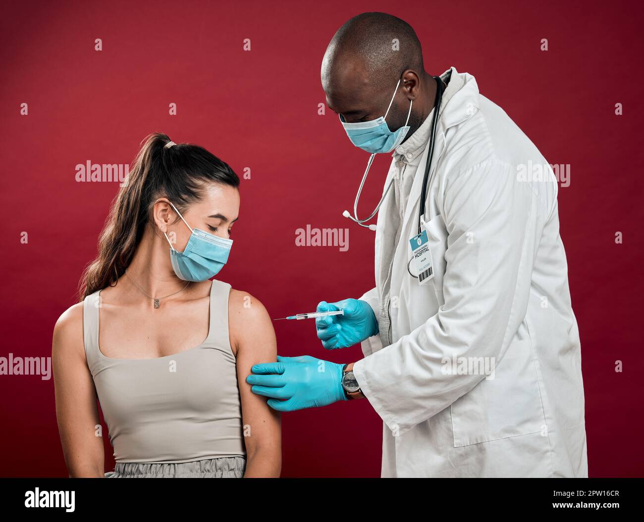 African american doctor giving covid vaccine to mixed race woman and wearing surgical face mask. Hispanic patient getting corona injection from physic Stock Photo