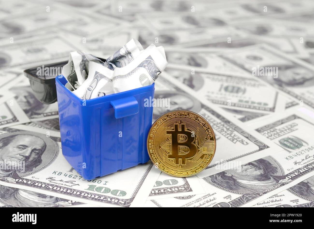 American cash notes are thrown into the trash bin at golden bitcoin on a multitude of hundred dollar bills. Senseless and thoughtless cash waste in th Stock Photo