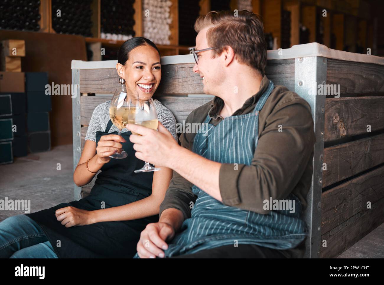 Successful distillery owners relaxing and celebrating with a glass of wine in the cellar or warehouse. Relaxed winemakers or employees enjoying an alc Stock Photo