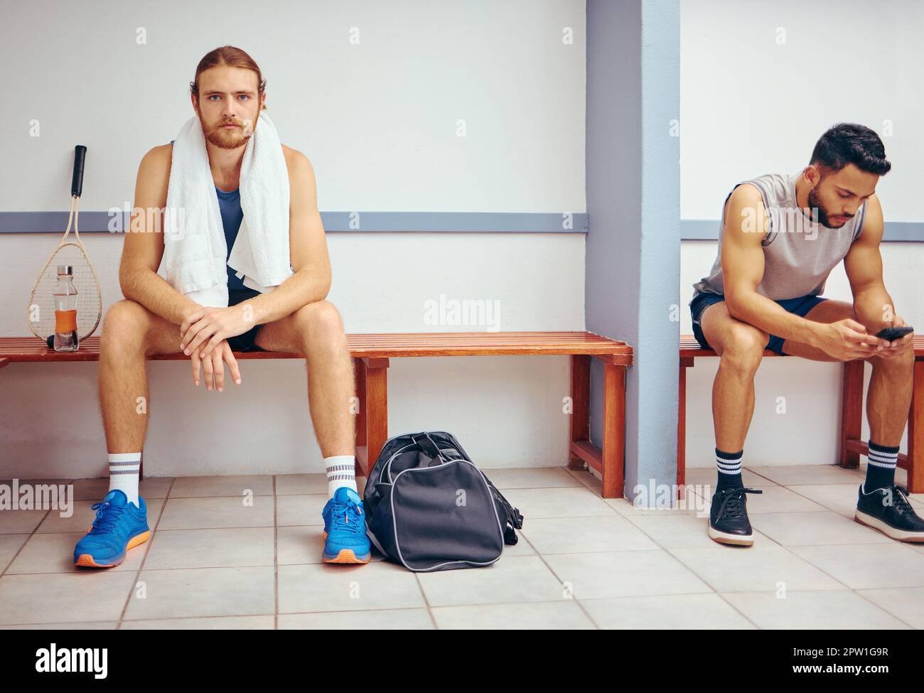 Portrait of a caucasian athlete sitting in a locker room. Two men sitting in a gym locker room together. Serious player relaxing in a gym together. Pr Stock Photo