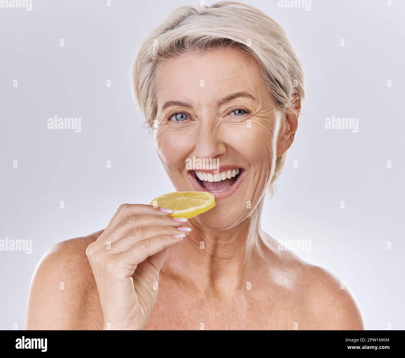 Health, nutrition and wellness of a mature woman happy in her aging skin care, beauty and face. Portrait of an old female model with a lemon promote a Stock Photo