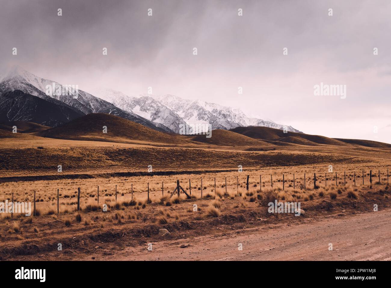Dry grassland with rolling hills by the snowy Andes mountains in Valle de Uco, Mendoza, Argentina, in a dark cloudy day. Stock Photo