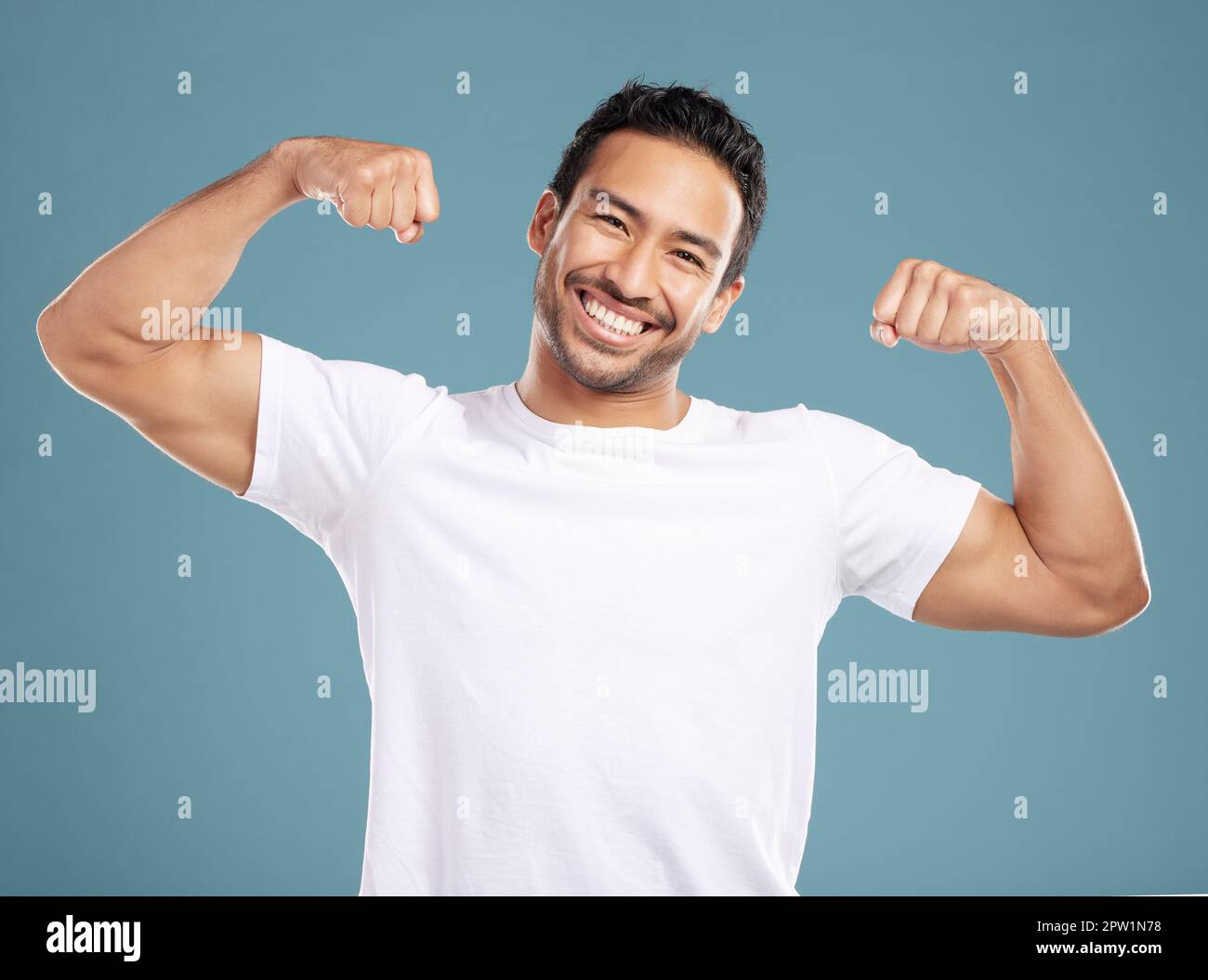 Handsome young mixed race man flexing his biceps while standing in studio isolated against a blue background. Athletic hispanic male showing his muscl Stock Photo