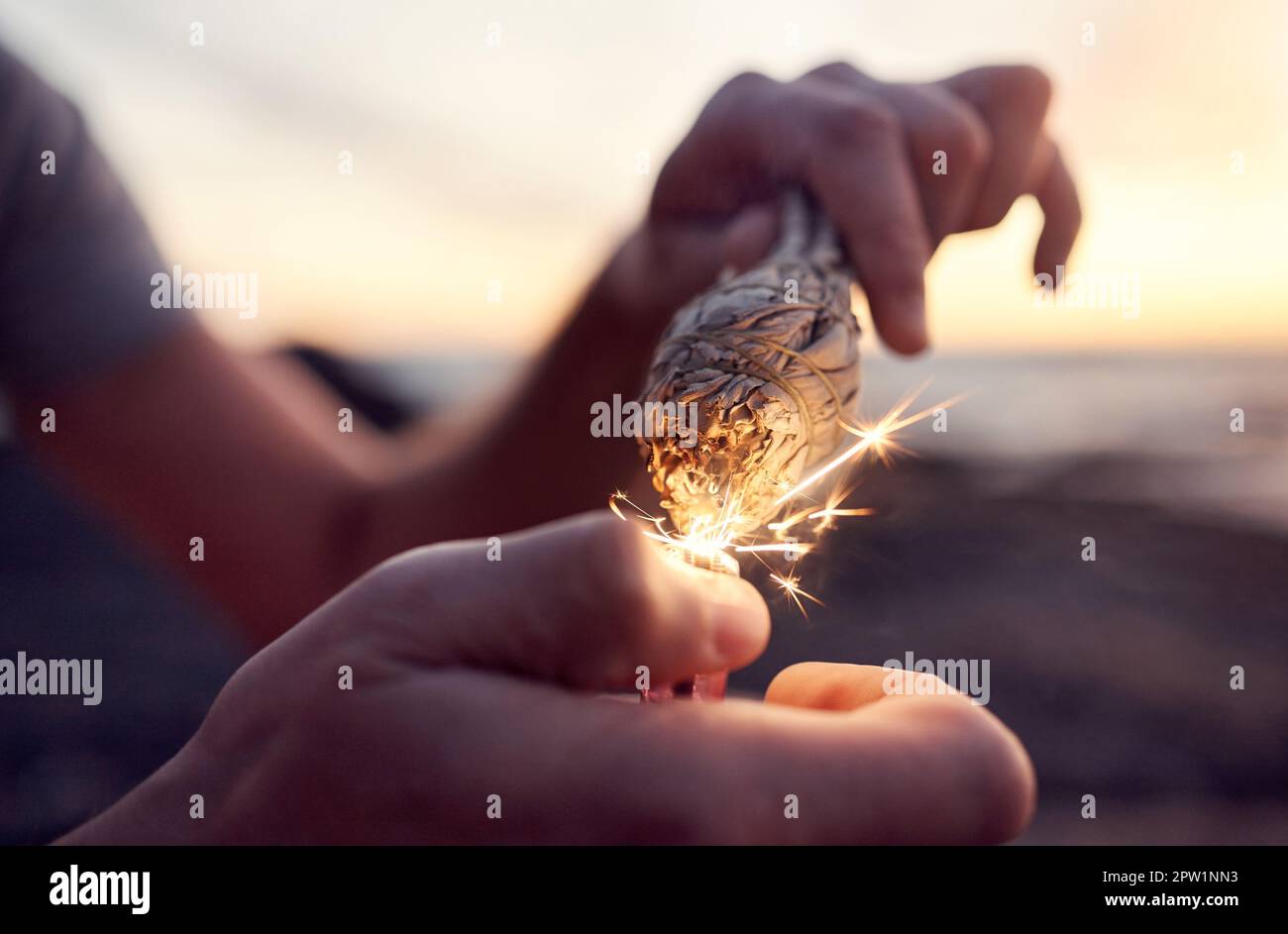 Hand, flame and sage burning at the beach for a spiritual ritual and