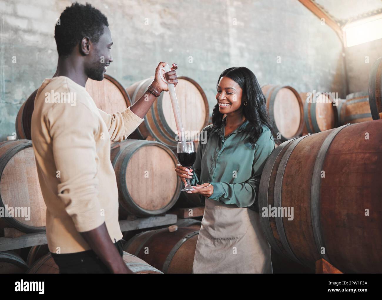 Wine tasting, couple and distillery farm worker serving red alcohol drink in glass with pipette in countryside. Happy smile, learning man and woman or Stock Photo