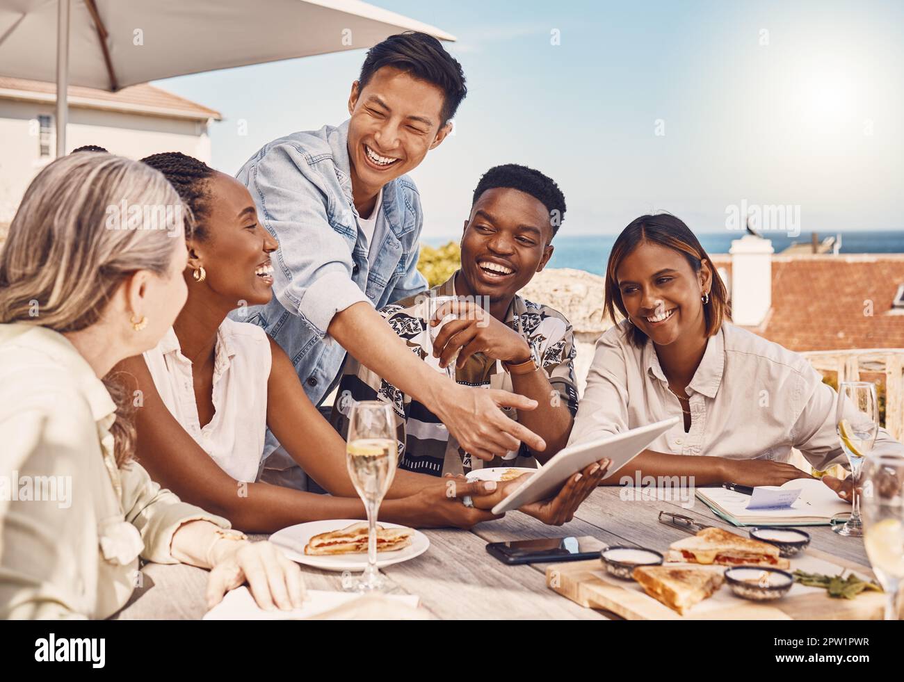 Friends, employees and casual workers at lunch meeting at restaurant, planning with 5g tablet and talking about marketing strategy while eating food a Stock Photo
