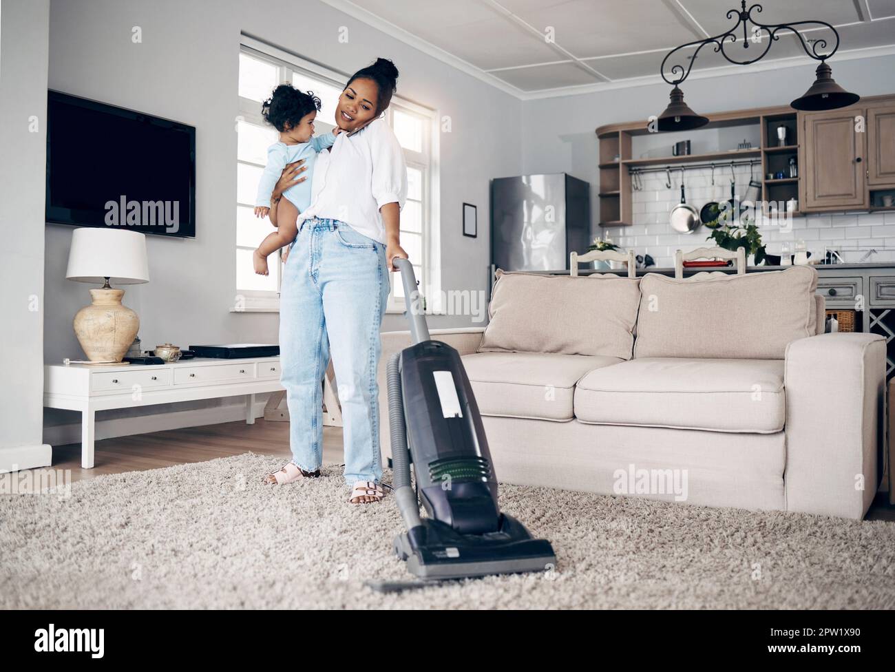 Shes mastered multi-tasking. a young mother using a cellphone while completing housework and holding her baby at home Stock Photo