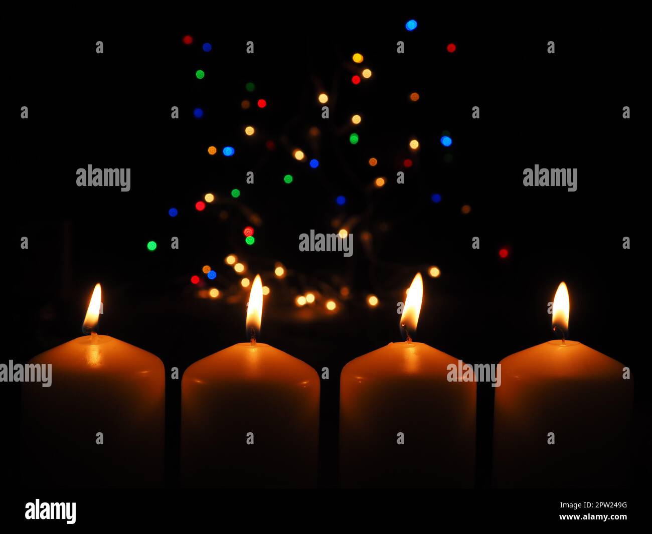 Four Advent candles burning with a colorful Christmas lights background