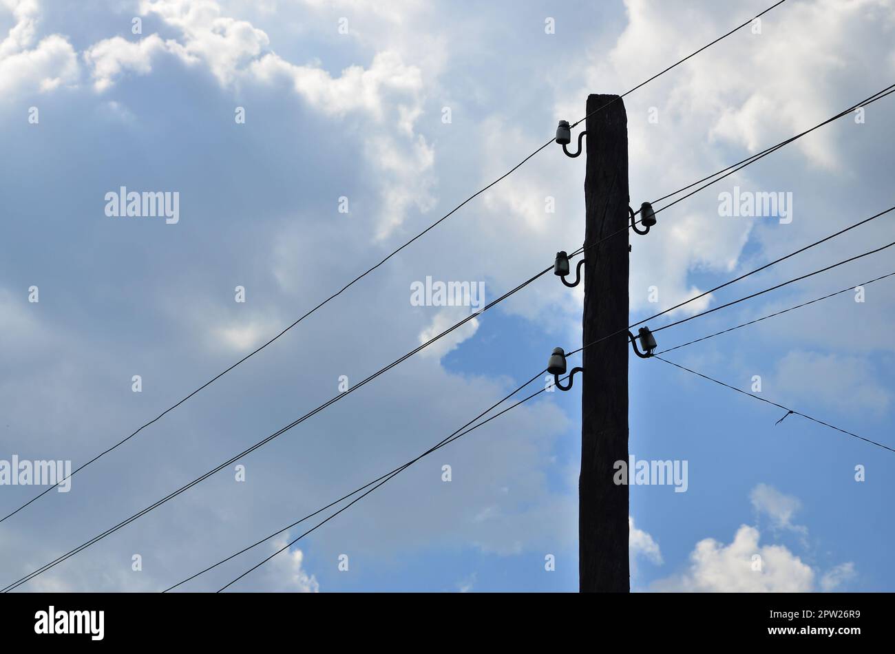 Old wooden electric pole for transmission of wired electricity on a background of a cloudy blue sky. Obsolete method of supplying electricity for late Stock Photo