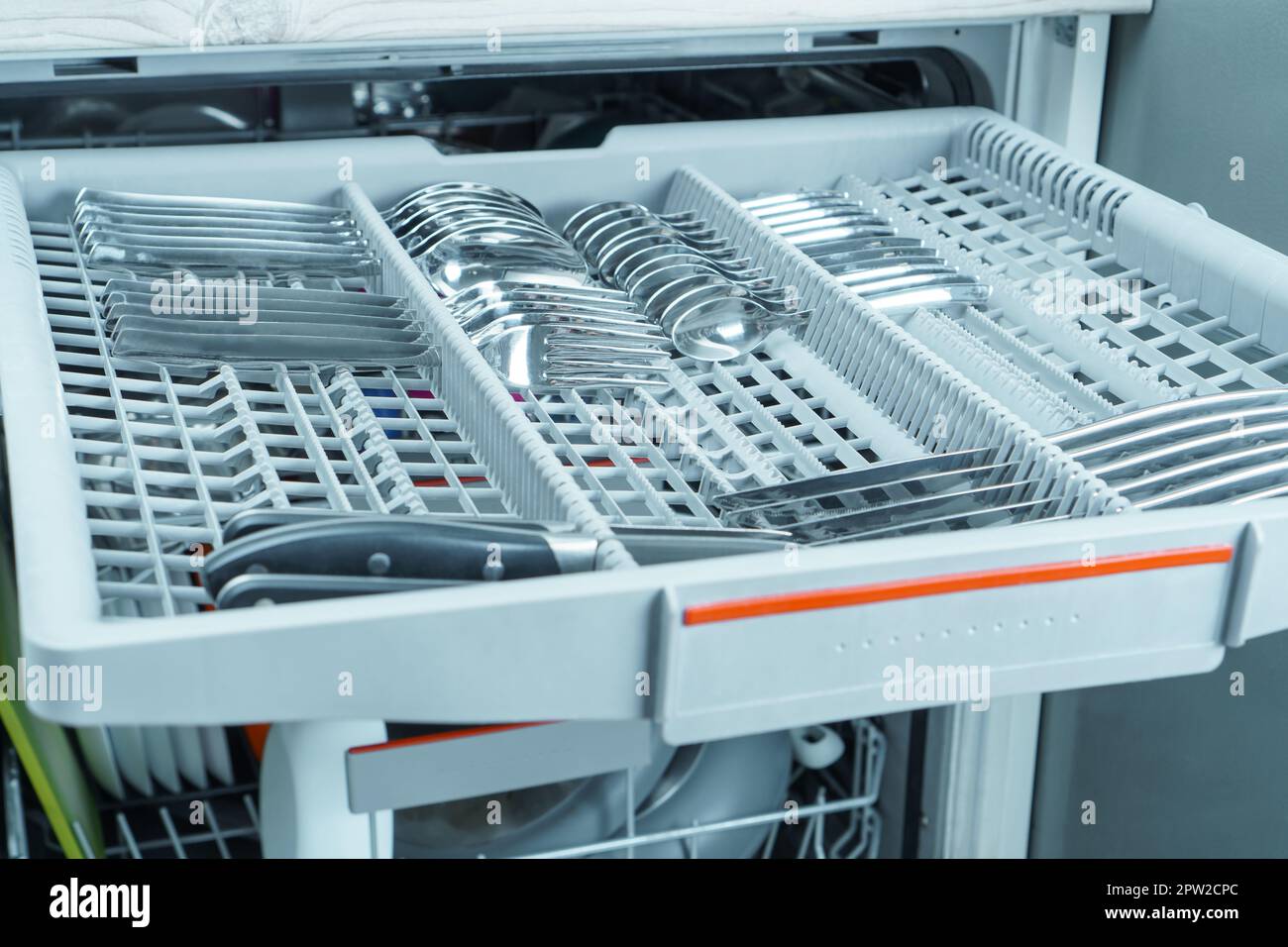 Closeup of grey compartment tray of open dishwasher machine with clean