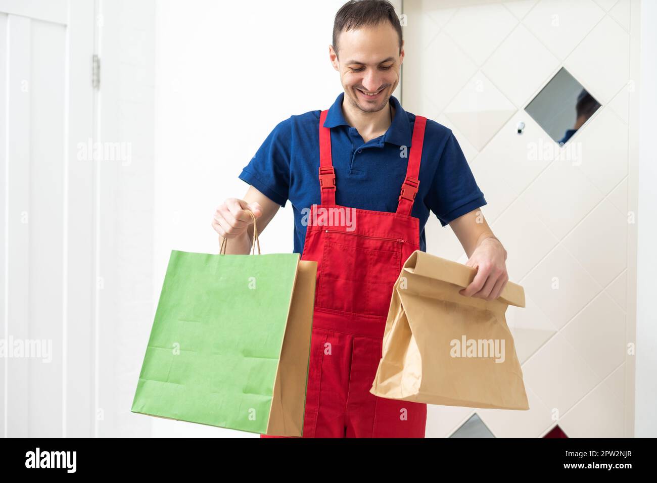 Image of a happy young delivery man in red cap standing with parcel ...
