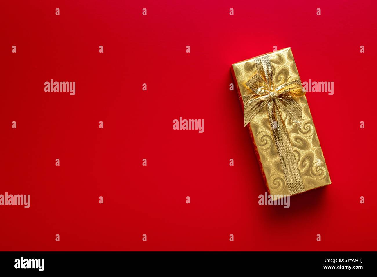 Gift wrapped in gold foil. Christmas present with gold ribbon on the red background. Top view. Stock Photo