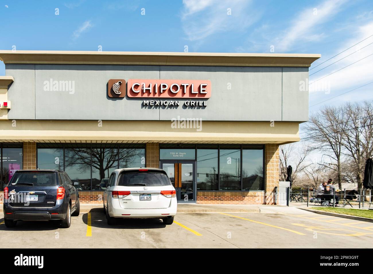 Exterior storefront and entrance of Chipotle Mexican Grill in a small strip mall. Two men eating outdoors. Wichita, Kansas, USA. Stock Photo