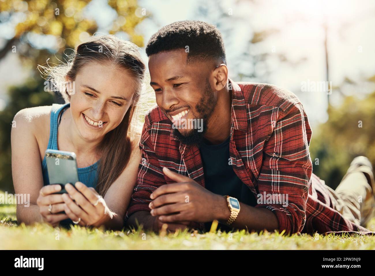 Interracial, couple and phone social media in park to relax, bond and smile together in Los Angeles. Technology, streaming and happy people enjoy summ Stock Photo