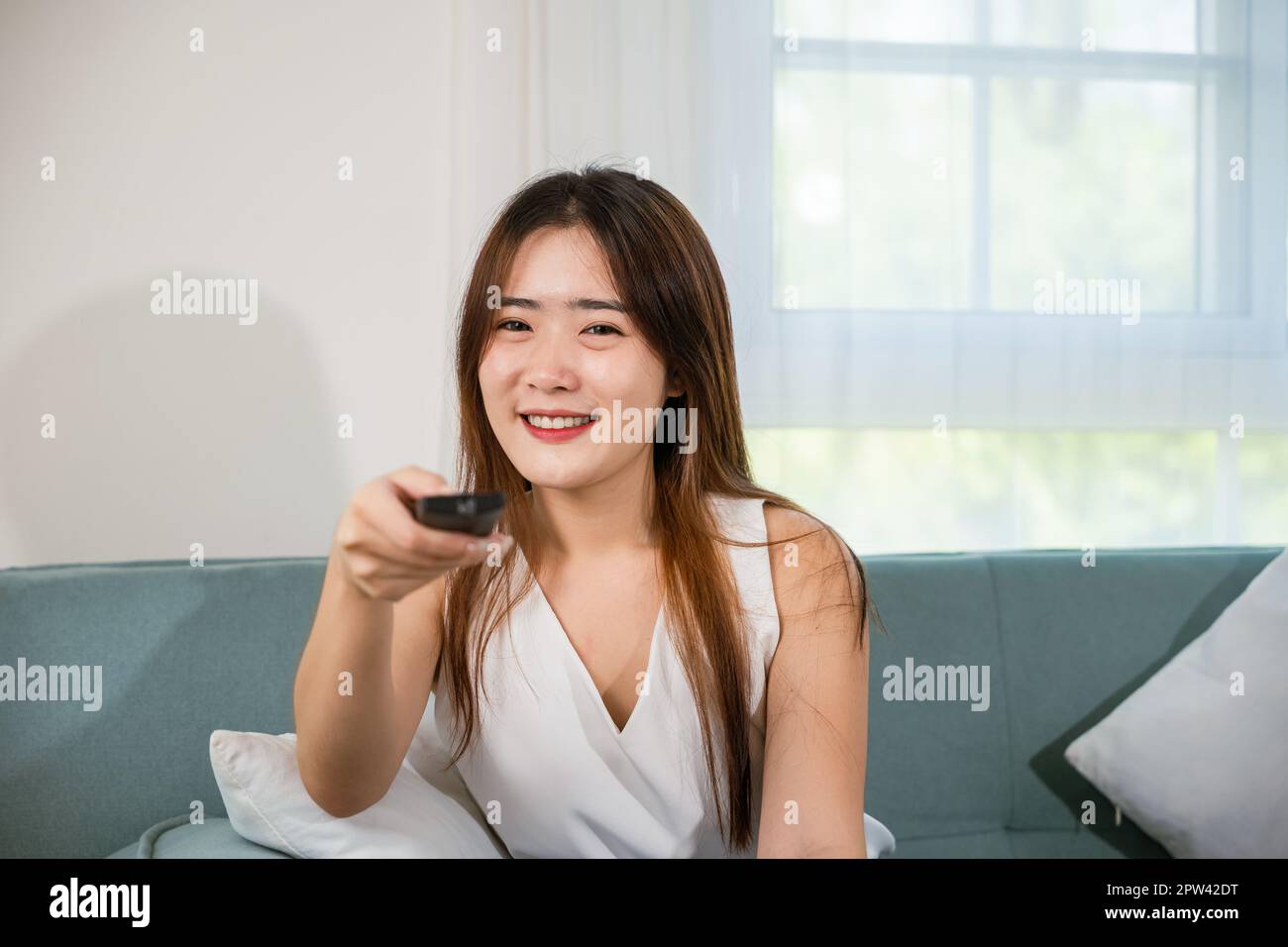 Beautiful female person look movie holding remote controller watching television, woman smiling sit relaxing watch TV hold remote control looking news Stock Photo