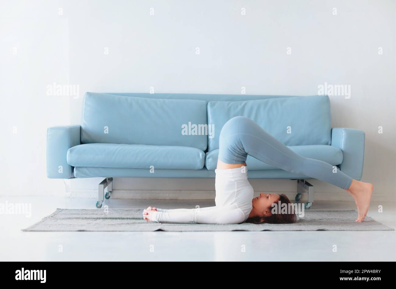 Slim female in sportswear bending aside while practicing yoga near sofa at home Stock Photo