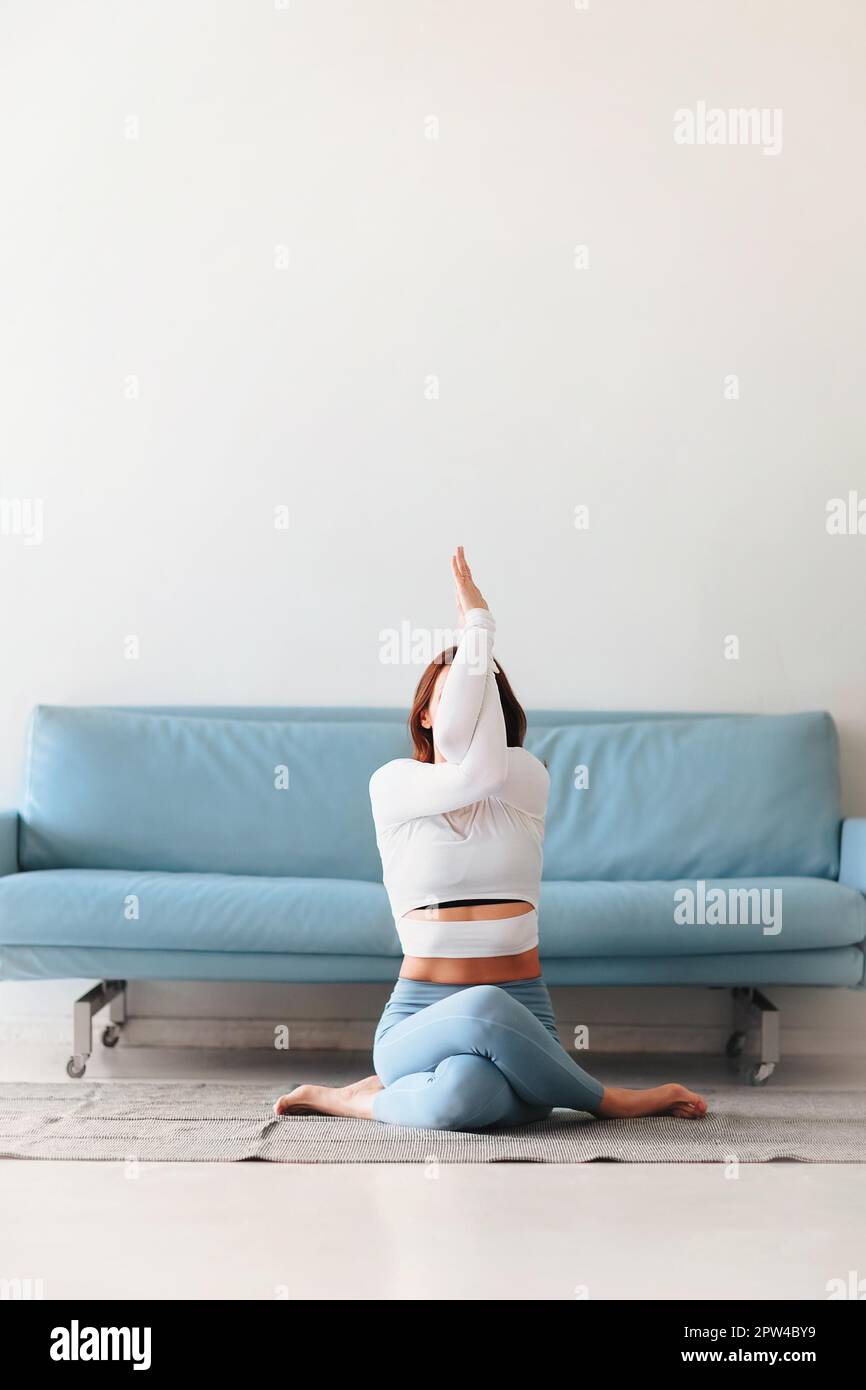Slim female in sportswear bending aside while practicing yoga near sofa at home Stock Photo