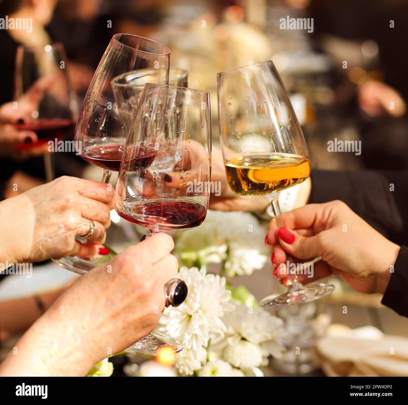 Group of crop anonymous friends clinking glasses with wine while gathering around table with delicious dishes and flower decoration during home dinner Stock Photo