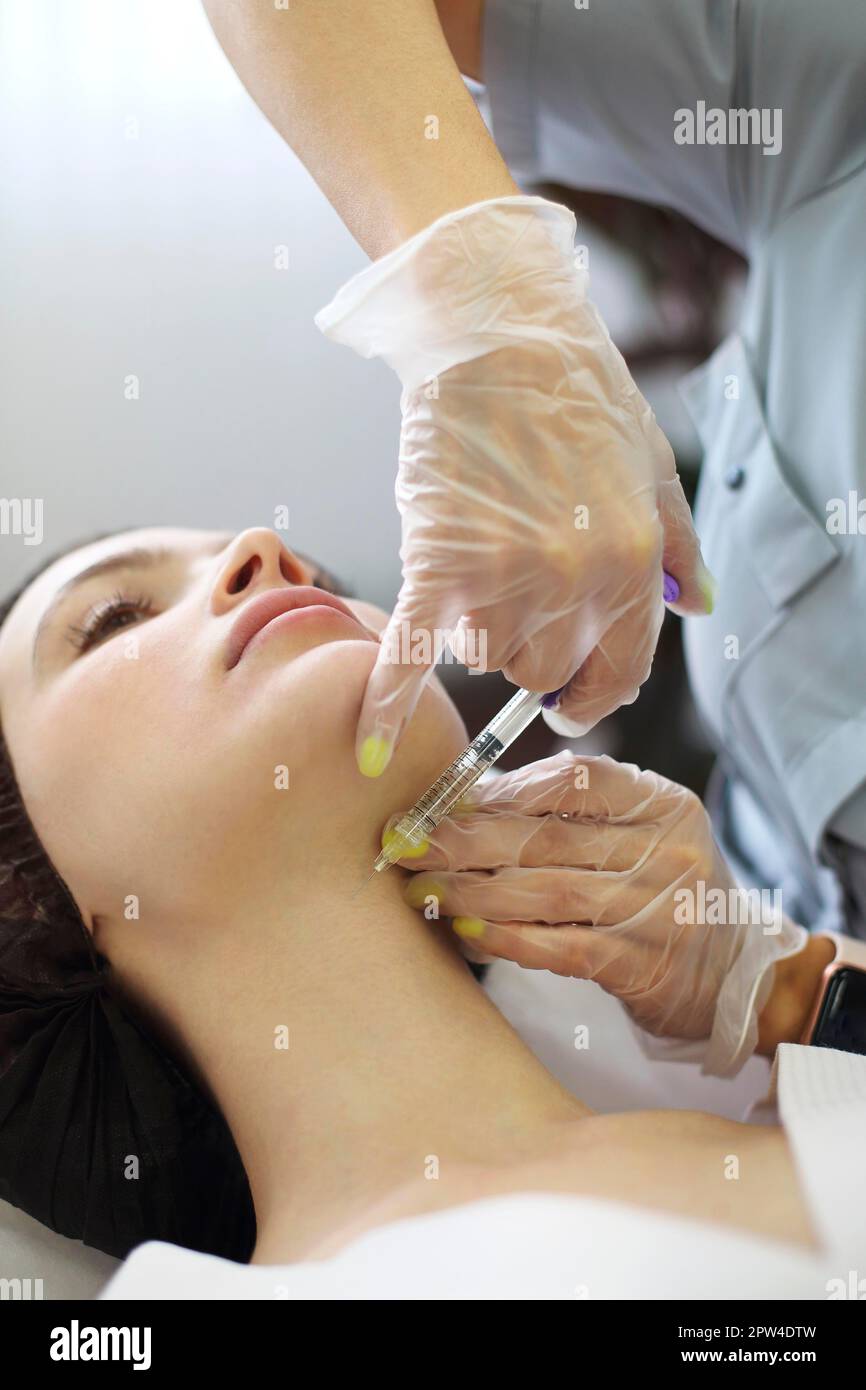 Professional beautician injecting hyaluronic acid near eyes of woman ...