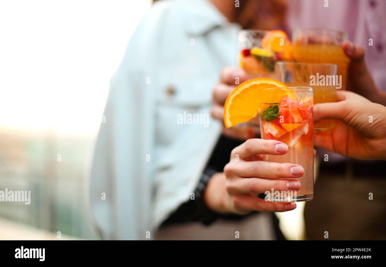 Happy men and women clinking glasses of fruit cocktails and proposing toast during the party Stock Photo