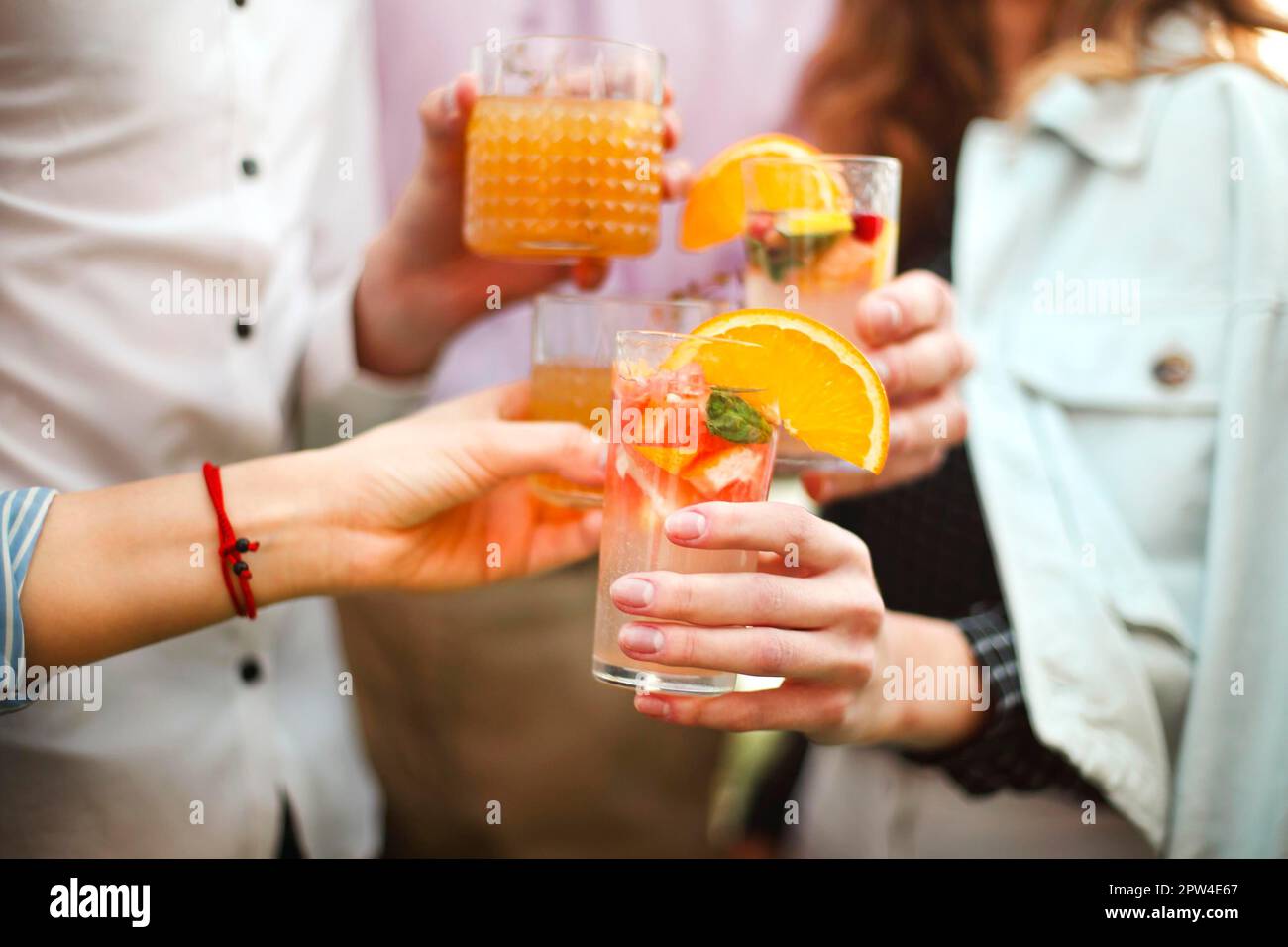 Happy men and women clinking glasses of fruit cocktails and proposing toast during the party Stock Photo