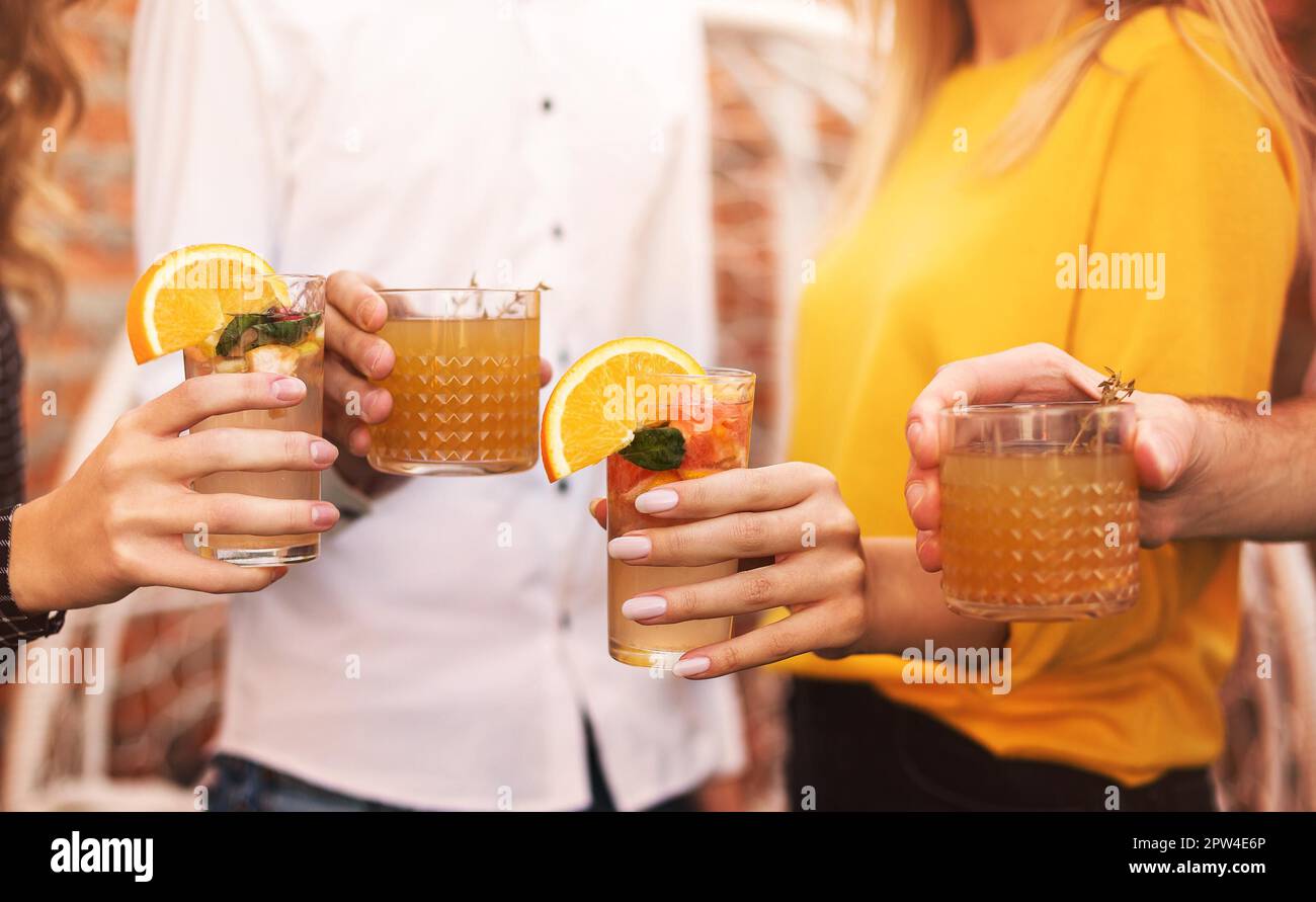 Happy men and women clinking glasses of fruit cocktails and proposing toast during the party Stock Photo