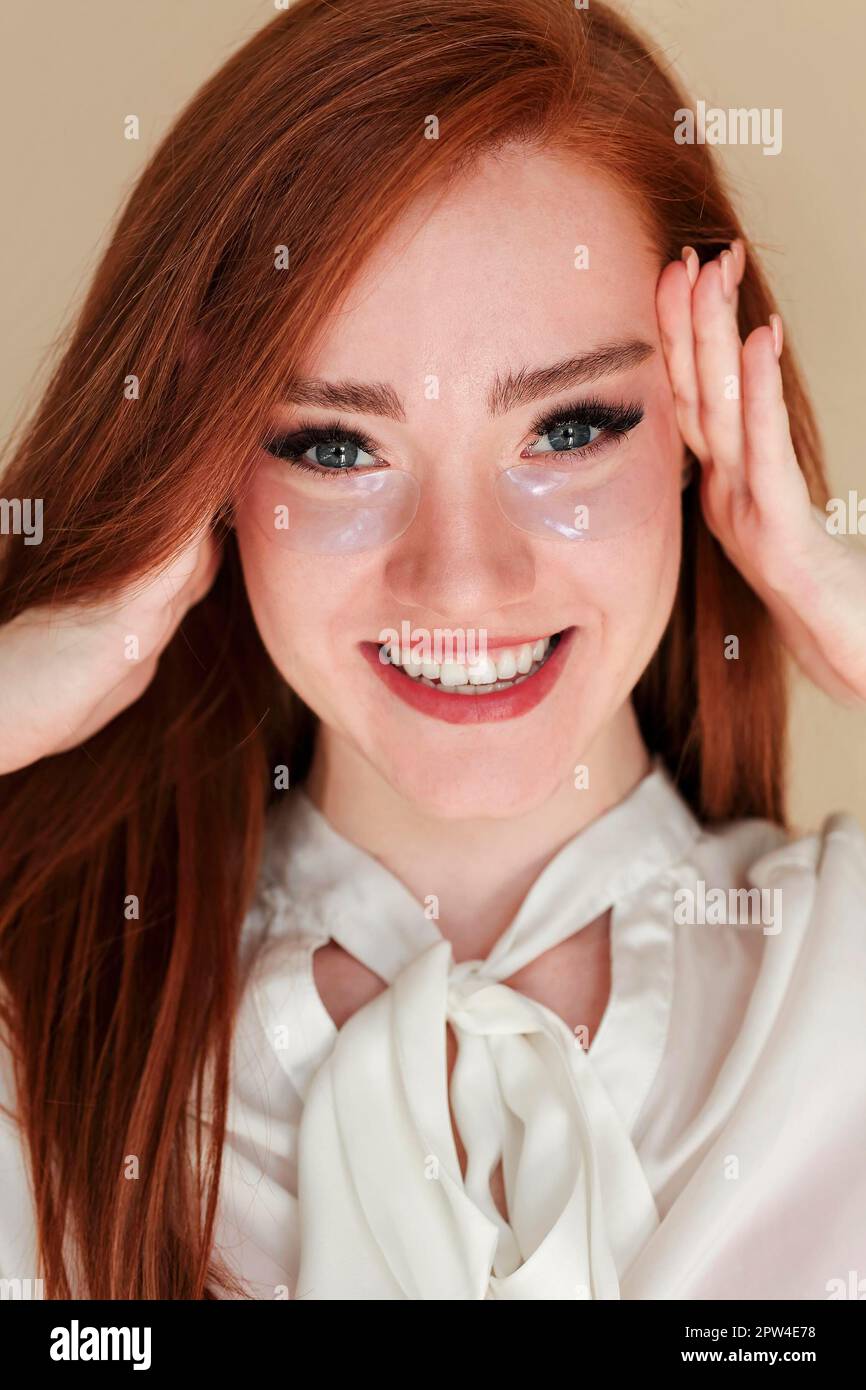 Cheerful young ginger woman with hydrogel eye patches touching head and