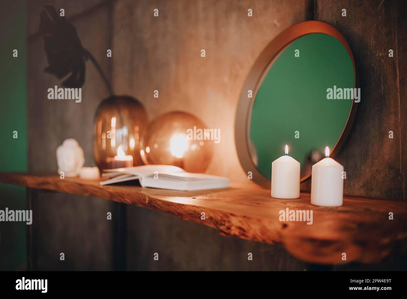 Round mirror on wooden shelf with two burning candles and small