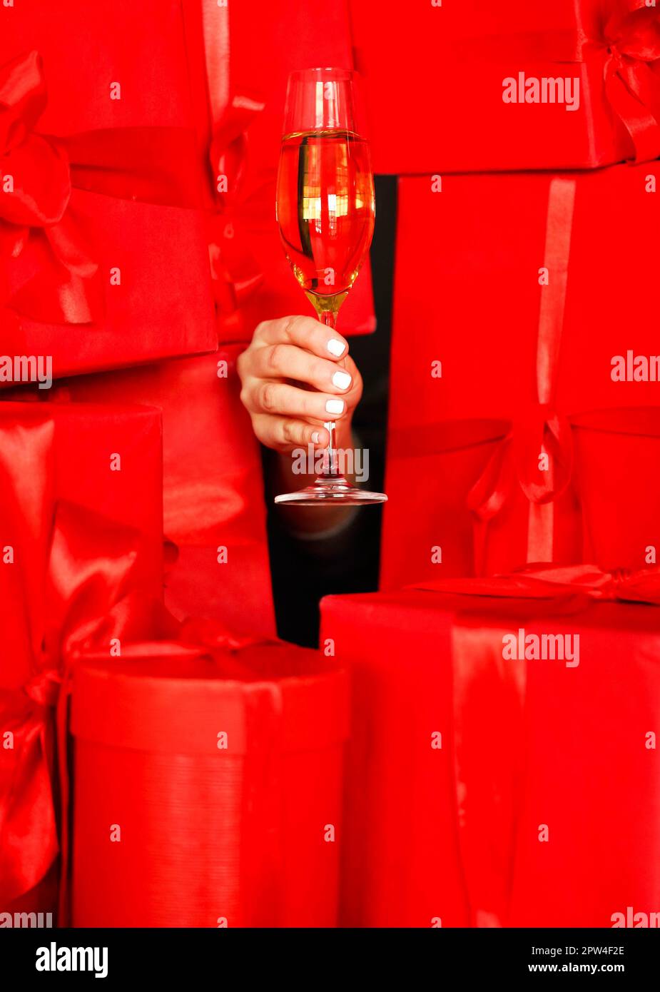 Unrecognizable female holding glass of champagne amidst red present boxes during Christmas celebration Stock Photo