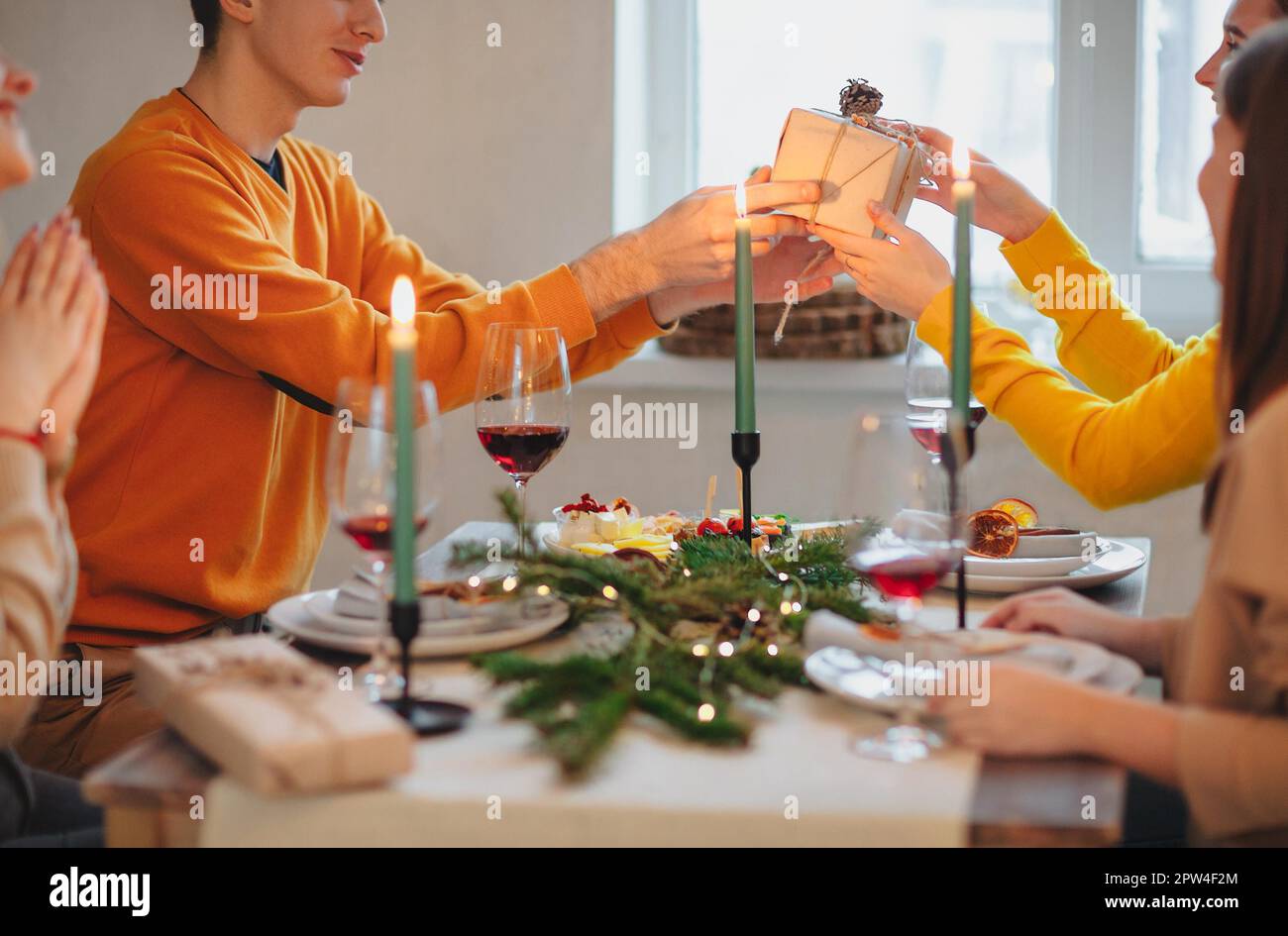 Happy person giving wrapped gift to friend while sitting at table and celebrating Christmas together Stock Photo