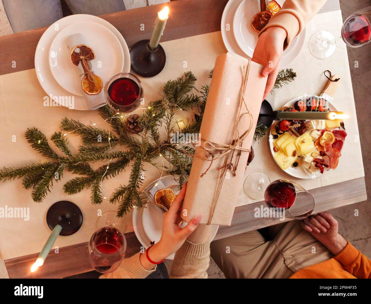 Happy person giving wrapped gift to friend while sitting at table and celebrating Christmas together Stock Photo